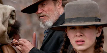 Rooster Cogburn, die zijn tas vastbindt, staat naast Mattie Ross